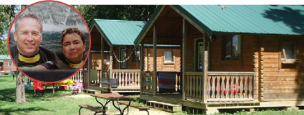 Cozy wooden cabins with green roofs at Crazy Horse Campground, featuring outdoor seating and a peaceful environment.