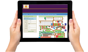 Hands holding a tablet displaying an online reservation system for booking camping sites with an interactive campground map.